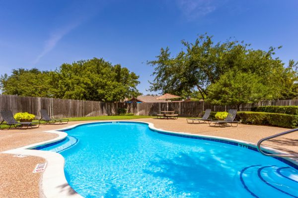 Quail Crossing apartments community pool with organic shape, sundeck, and large trees nearby